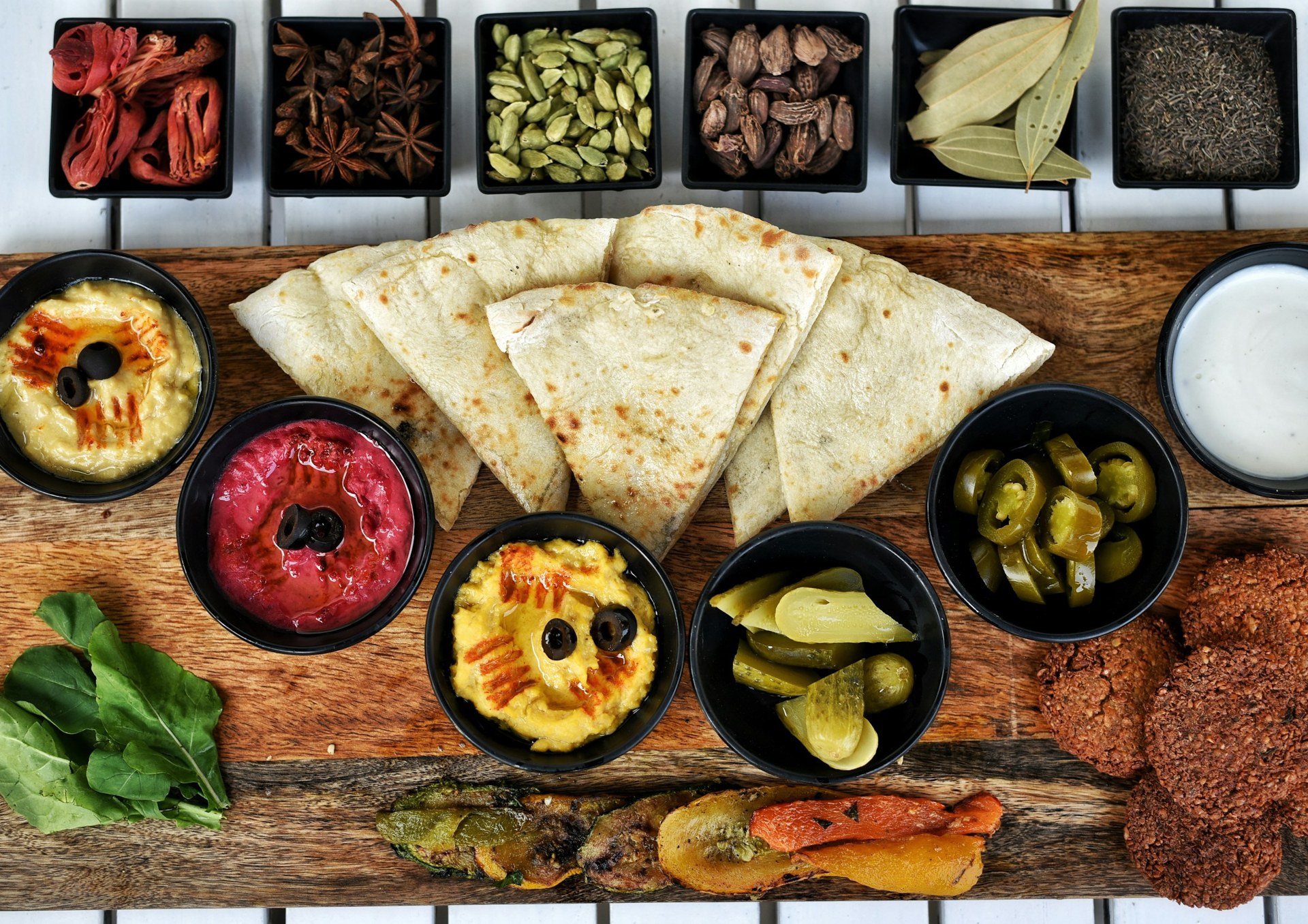 A mezze board: hummus, beetroot hummus, flatbread, pickles, jalapeños, a yoghurt dip and falafel, with whole spices
